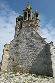 Pignon sans ouverture, à part trois minuscules meurtrières à gauche. En haut, il se transforme en clocher, couronné d'une toute petite flèche. Deux tourelles de part et d'autre de ce clocher.