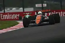 Photo d'une monoplace bleue et orange vue de l'avant, sur une piste de course