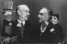 Photographie en noir et blanc de deux hommes avec leurs marionnettes.