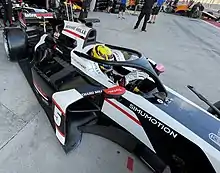 Photographie d'une monoplace de F2 noire et blanche, de trois-quarts gauche, dans la voie des stands.