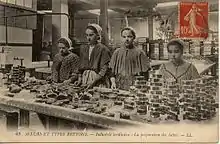 Quatre jeunes filles debout devant une table couverte de boîtes à sardines vides.