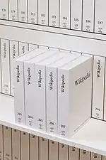 Plusieurs livres blancs à la typographie sobre, rangés verticalement, dont les tranches et la couverture de l'un d'entre eux sont lisibles