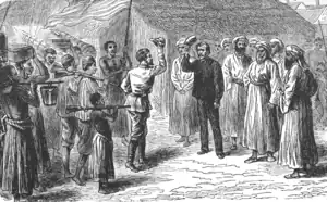 deux hommes blancs se saluent ; ils sont entourés d'hommes habillés de djellabas et d'autres, vêtus de pantalons et chemise ou de pagnes, portant pour certains un fusil sur l'épaule ou un panier sur la tête. L'arrière-plan est celui d'une habitation à toit de chaume