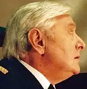 Un homme aux cheveux blancs en uniforme militaire, regardant au-dessus de son épaule gauche.