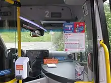 Photographie en couleurs de l'espace conducteur d’un minibus, avec un plexiglas et un distributeur de gel hydroalcoolique le séparant des passagers.