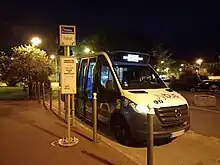 Photographie nocturne en couleurs d’un minibus bleu, blanc et noir stationné à un arrêt de bus