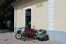 Photographie en couleurs d'un bâtiment de location de vélos J'yvélo devant lequel sont alignés plusieurs vélos.