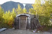 Une cabane dans une forêt, avec des montagnes en arrière-plan.