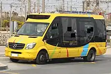 Photographie en couleurs d’un minibus jaune et noir, avec des installations ferroviaires en arrière-plan.