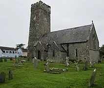 Photo d'un bâtiment allongé aux murs de pierre grise et au toit en ardoises avec une grande tour carrée crénelée munie d'une horloge
