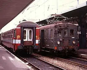 Photo couleur de l'arrière d'une voiture de train couleur rouge vif à bandeau gris très clair sous la zone des baies.