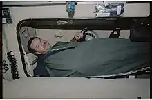 Photographie d'un homme dans un sac de couchage, en apesanteur.