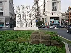 Photographie en couleurs d'un alignement de blocs maçonnés sur un terre-plein engazonné.