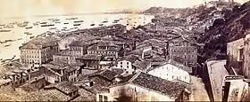 Vue plongeante du sommet d'une colline donnant sur les immeubles d'une ville avec un port encombré de divers navires en arrière-plan
