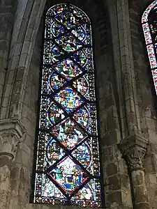 Vitrail composé de pièces rectangulaires et triangulaires. Sont représentés différents personnages dans plusieurs scénettes, difficilement visibles en raison du noircissement du vitrail.