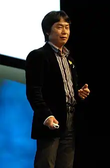 Photo d'un homme d'origine asiatique debout en costume noir et légèrement souriant.