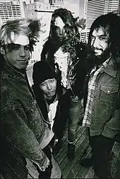 Photographie noir et blanc de trois hommes debout et un homme assis sur le toit d'un immeuble.