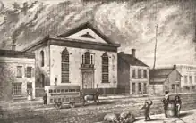 Bâtiment néo-classique. Un tramway hippomobile passe devant le bâtiment, au premier plan, un homme frappe une truie avec une verge pour qu'elle ne fouille pas dans des ordures.