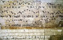 Notations musicales peinte sur un mur de pierre (en partie effacées).