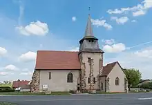 Vue de l'église Saint-Martial : on voit la nef à côté du clocher à flèche. Juste à côté du bâtiment, on distingue un monument au mort qui jouxte la route.