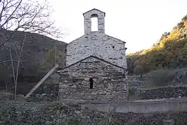 Mur en pierres percé d'une petite fenêtre en arc, surmonté d'un toit. Plus haut derrière, autre mur surmonté d'un clocher-mur.