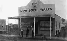 Photographie noir et blanc d'un bâtiment d'un seul étage avec une devanture où est inscrit Bank New South Wales.