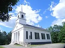 église blanche avec un haut clocher et des piliers à l'avant.