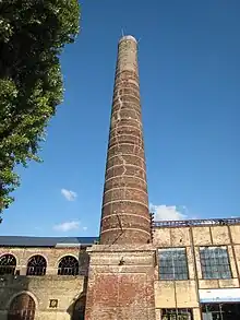 Cheminée de briques de la sucrerie de Francières haute de 33 mètres. Derrière, la halle dite "Thirial", bâtiment en briques de 1829.