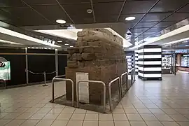 Photographie en couleurs d'un mur de pierres ancien dans un hall commercial.