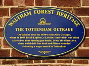 Photographie en couleurs d'une plaque commémorative bleue et jaune sur un mur de briques.