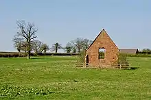 Photo d'un petit bâtiment en briques rouges entouré d'une barrière. On peut voir le paysage derrière à travers une fenêtre