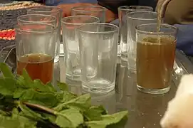 Un verre à moitié rempli, plusieurs verres vides, un verre en train d'être rempli de thé dans lequel se trouvent de nombreux résidus.