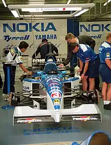 Vue d'une monoplace bleue et blanche devant un garage.