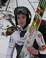 portrait tête et épaules de Urša Bogataj avec son casque et ses skis à la main, devant la piste de réception du tremplin de Brotterode