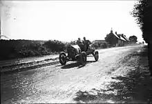Photo d'un homme et d'un passager assis dans une voiture entourée par le public.