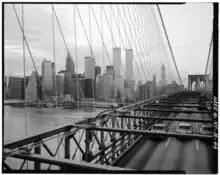 Photo en noir et blanc de trois voies empruntées par des voitures sur un pont à haubans. En arrière-plan, la rive d'un dense quartier de grattes-ciel.