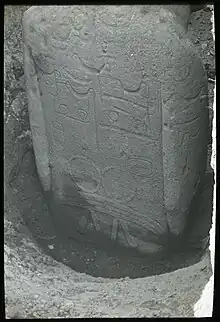 Photographie d'un moai à moitié enterré. Le dos de la statue est recouverte de motifs typiques des tatouages.