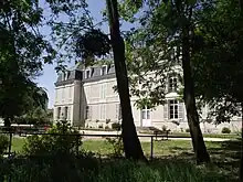 Photographie d'un bâtiment blanc vu à travers des arbres.