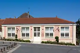 Vue d'un bâtiment bas à la façade rose et aux grandes baies à petits carreaux.