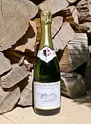 Photographie couleur d'une bouteille de vin mousseux posée devant un tas de bois.