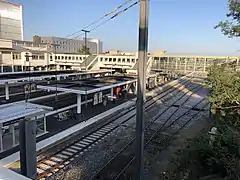 Vue sur les voies, la passerelle et la gare en arrière plan.