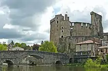 Photographie du château de Clisson prise en avril 2009 depuis la rive sud est opposée ; les hautes ruines se détachent sur fond de ciel nuageux ; au premier plan coule la Sèvre nantaise enjambée par un pont de pierre.