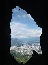 Agglomération cernée de montagnes vue « en médaillon » au travers des parois d'une grotte.