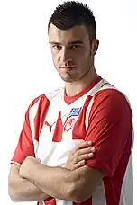 Photographie d'un joueur de football posant avec un maillot rouge et blanc.