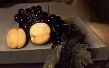 Peinture de deux pêches posées sur une table en pierre, accompagnées d'une grappe de raisins rouges.