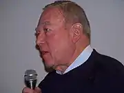 Homme âgé de profil parlant dans un micro.